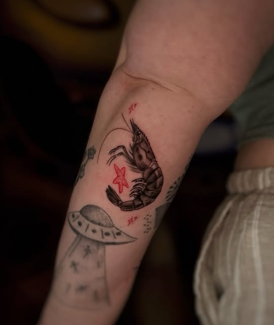 Fine black and red shrimp tattoo on an inner arm