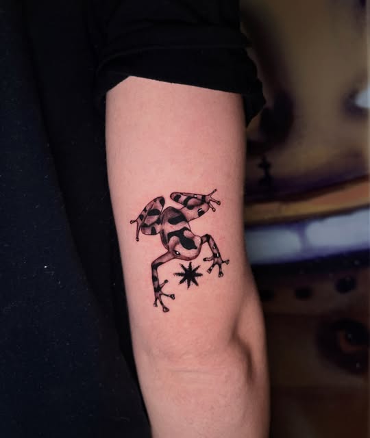 Small blackwork frog tattoo on an upper arm